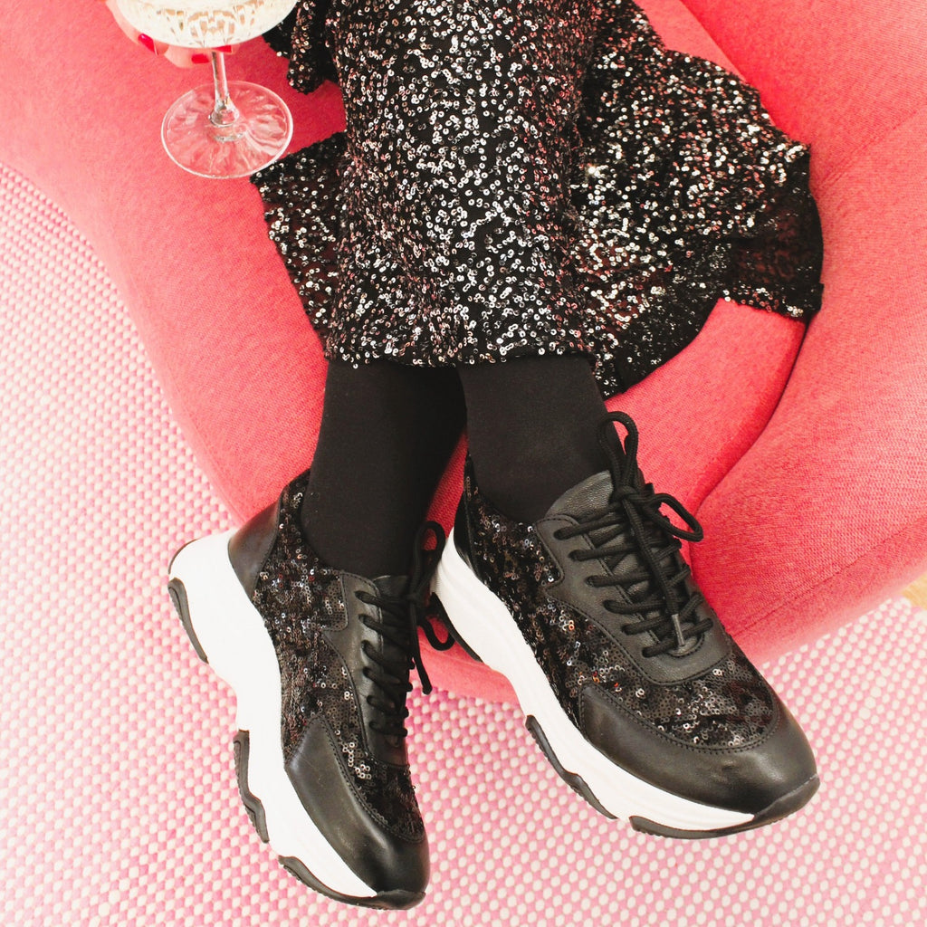 En rosa soffa ett par fötter med svarta glittiga sneakers The Shoe Bakery